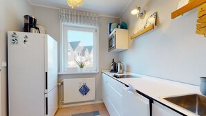 Et moderne køkken med hvide skabe, en indbygget ovn, en mikroovn og et vindue med udsigt til huse.