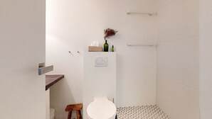 Et lille, moderne badeværelse med toilet, en træskammel, en hylde med en vase og et håndklædetørrestativ.