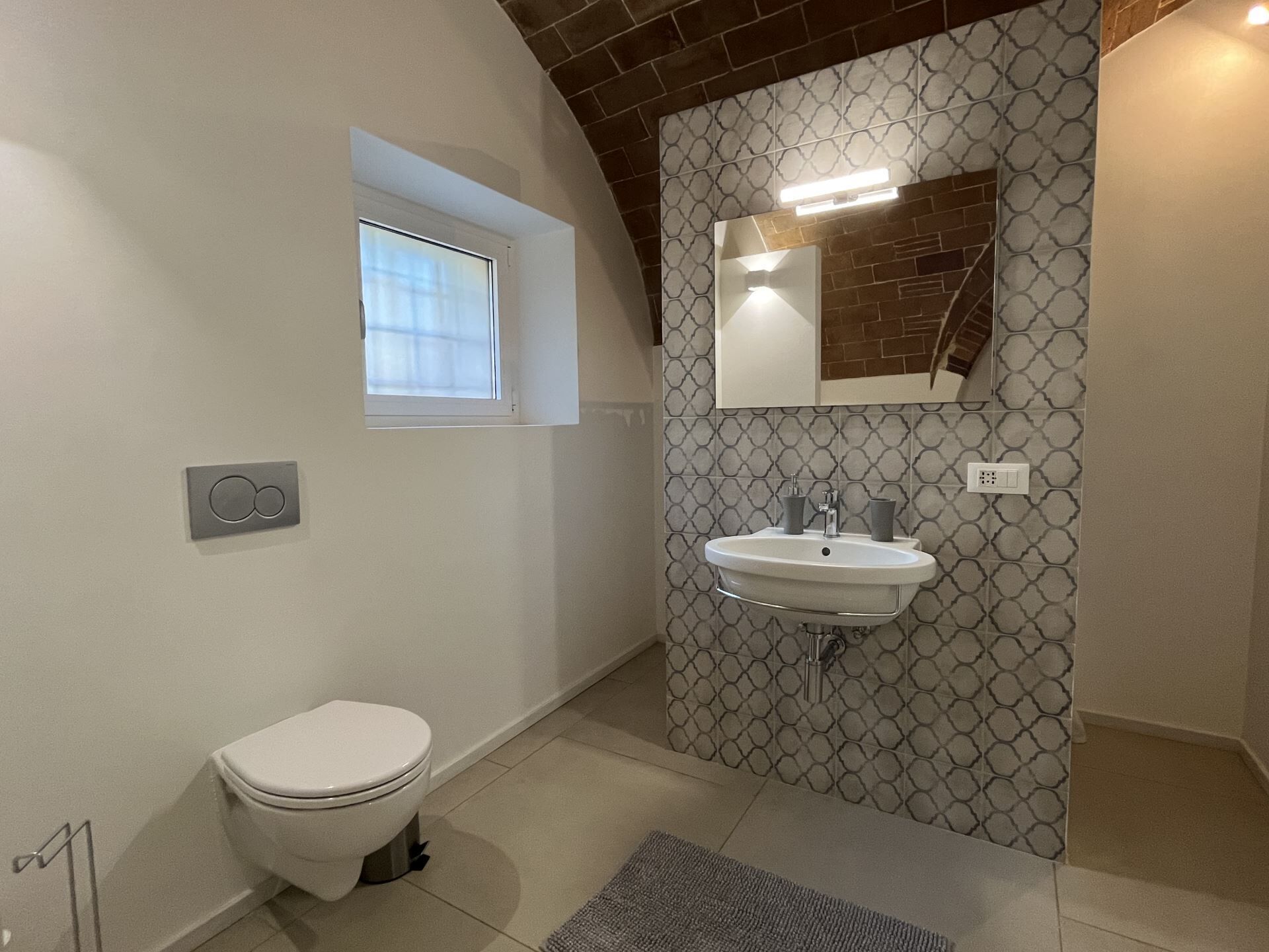 Un baño con inodoro, lavamanos, ventana y paredes con diseño.