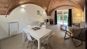A dining area with a white table and chairs, a television, and a small wooden stool. - San Gaetano apartment in Follonica (Follonica)