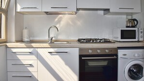 Una cocina moderna con armarios blancos, un lavaplatos de acero inoxidable, una estufa a gas, un microondas, un horno y una lavadora.