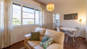 Un espacio de sala acogedor con sofá, mesa de comedor y sillas. Un amplio ventanal ofrece vistas al exterior.