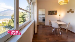 Una cocina moderna con armarios blancos, un comedor con mesa y sillas redondas, y vistas a un cuerpo de agua y montañas a través de ventanas amplias.