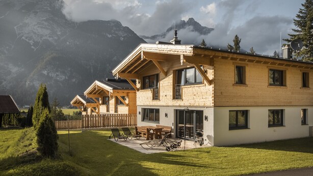 A chalet-style building with a wooden exterior, large windows, and a patio area with outdoor seating. - Wilderer Chalets (Leutasch)