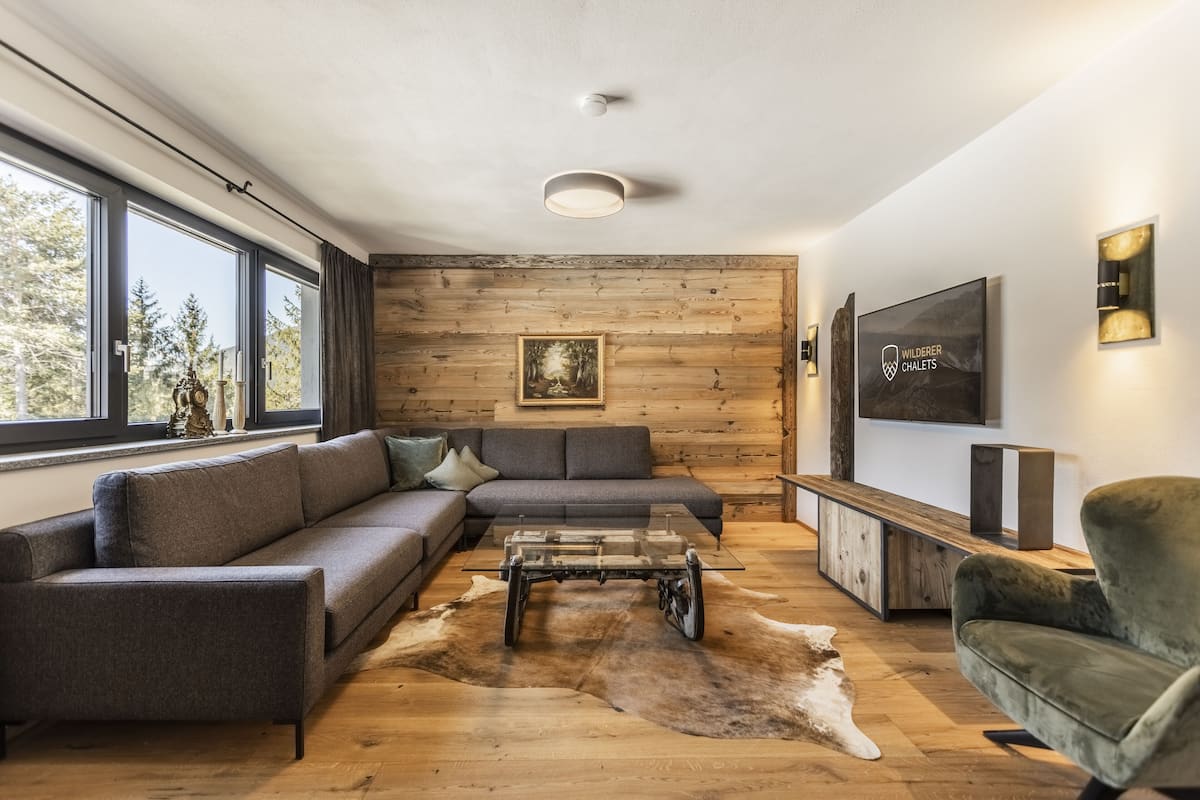 A modern living room with a wooden wall, a sofa, a glass coffee table, and a leather rug.