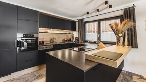 A modern kitchen with black cabinets, a central island, and a window with natural light. - Wilderer Chalets (Leutasch)