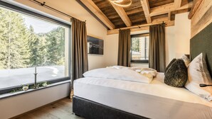 A bedroom with a large bed, wooden ceiling beams, a window with curtains, and a sign on the wall. - Wilderer Chalets (Leutasch)