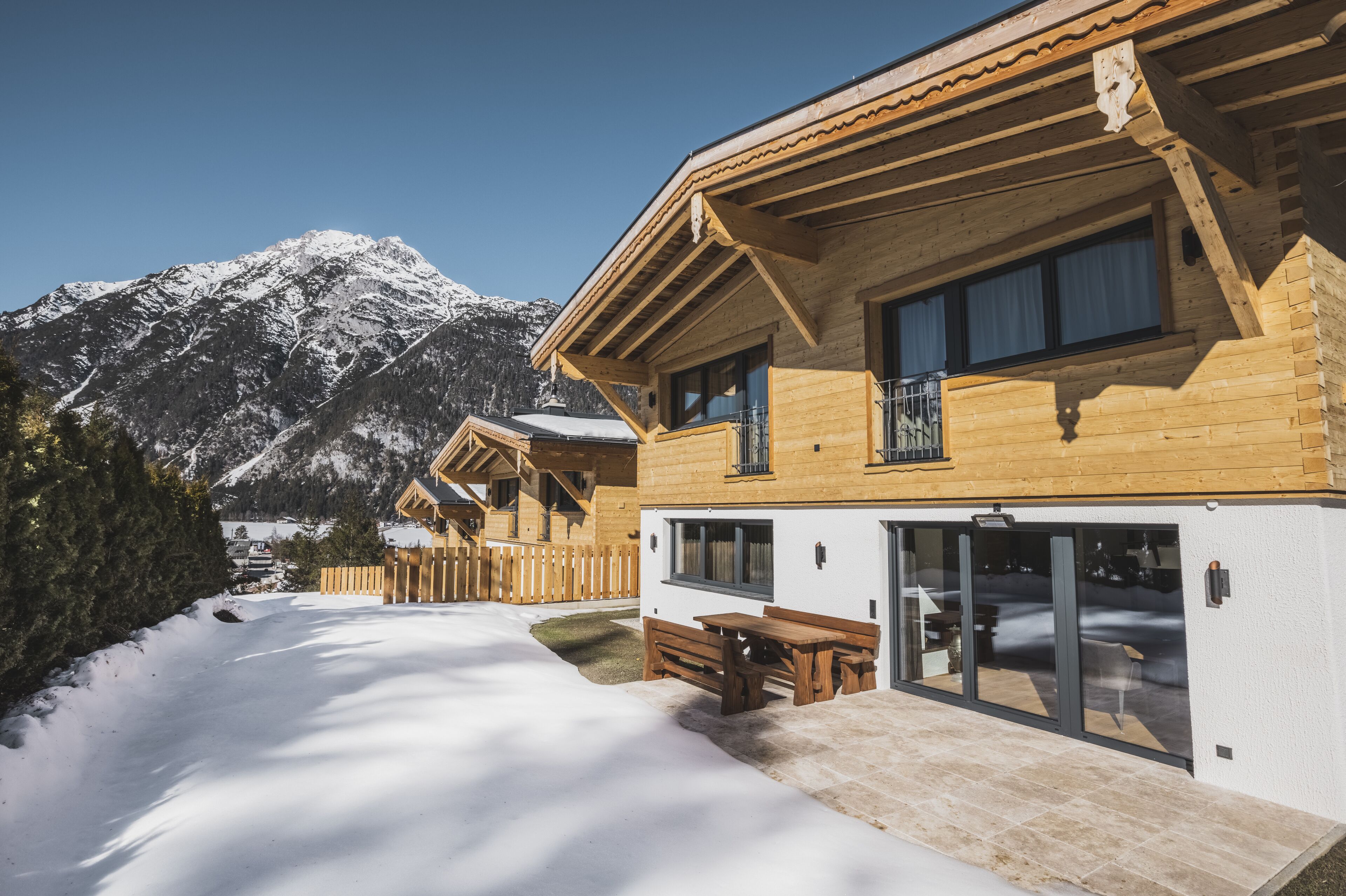 A wooden chalet with a patio and a view of snow-covered mountains.