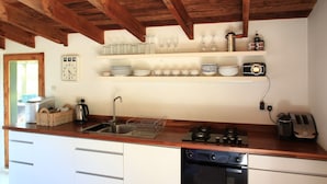 Une cuisine avec des meubles blancs, un plan de travail en bois, un four encastré et une horloge au mur.