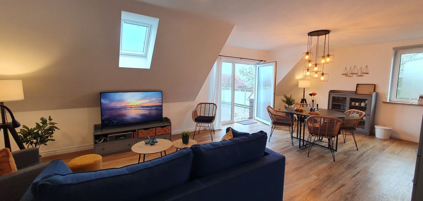 Una sala de estar moderna con televisor, sofá, mesa de comedor y sillas.