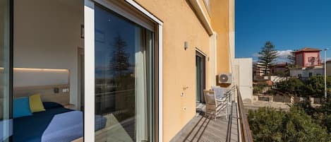 Habitación de hotel moderna con un amplio ventanal corredero que da a un balcón, una cama con ropa de cama azul y vistas del entorno.