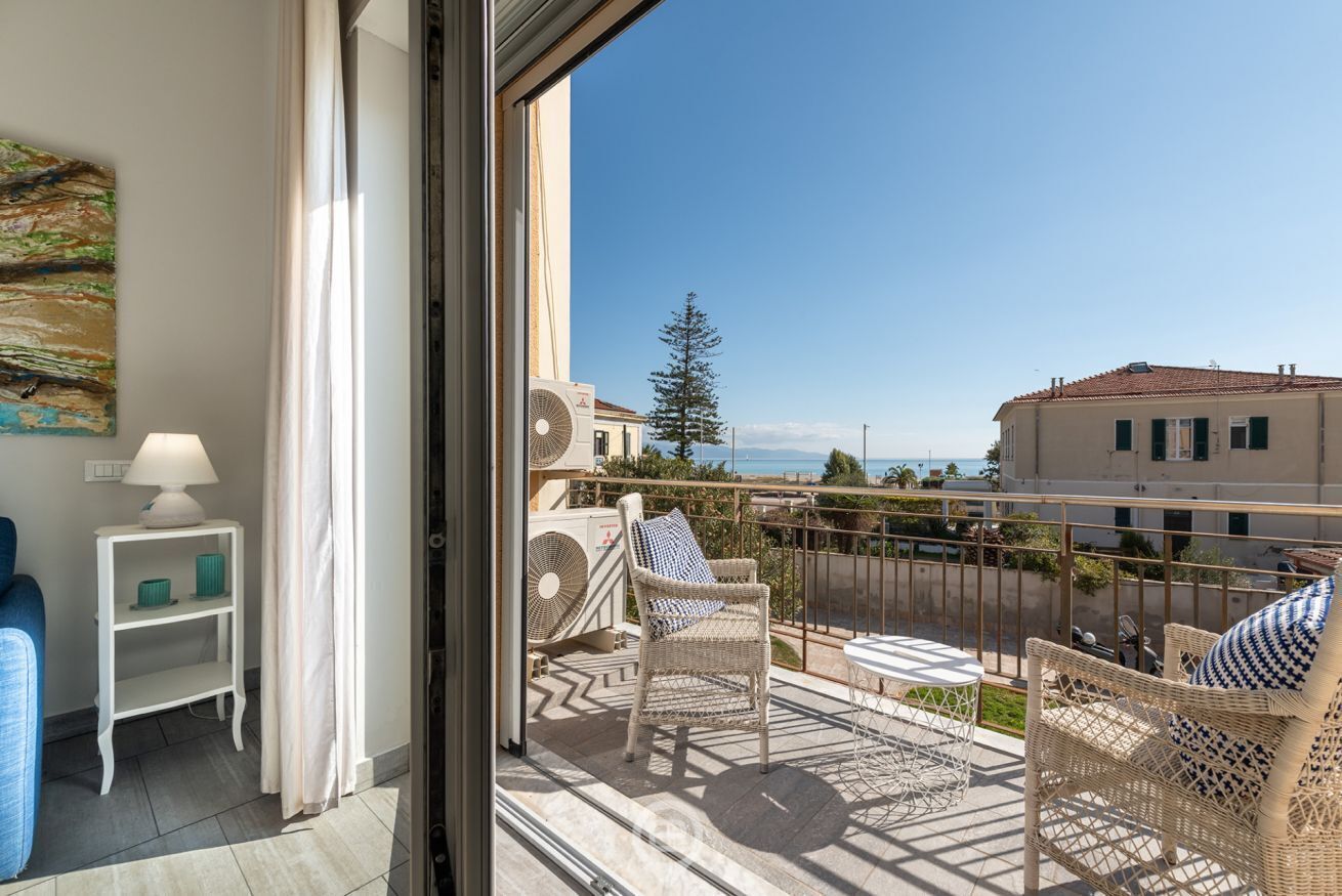 Un balcone con mobili in vimini, un tavolo e vista sul mare e sugli edifici.