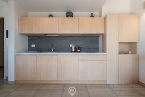 A modern kitchen with light wood cabinets, a grey backsplash, and a stainless steel range hood.