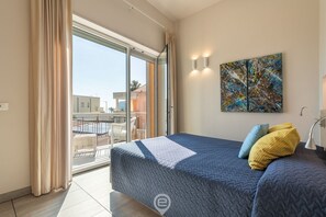 Een slaapkamer met een groot bed, een balkon met uitzicht en een schilderij aan de muur.