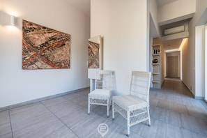 Um interior moderno com duas cadeiras de vime branco, uma grande pintura abstrata e um corredor que leva a outro cômodo.