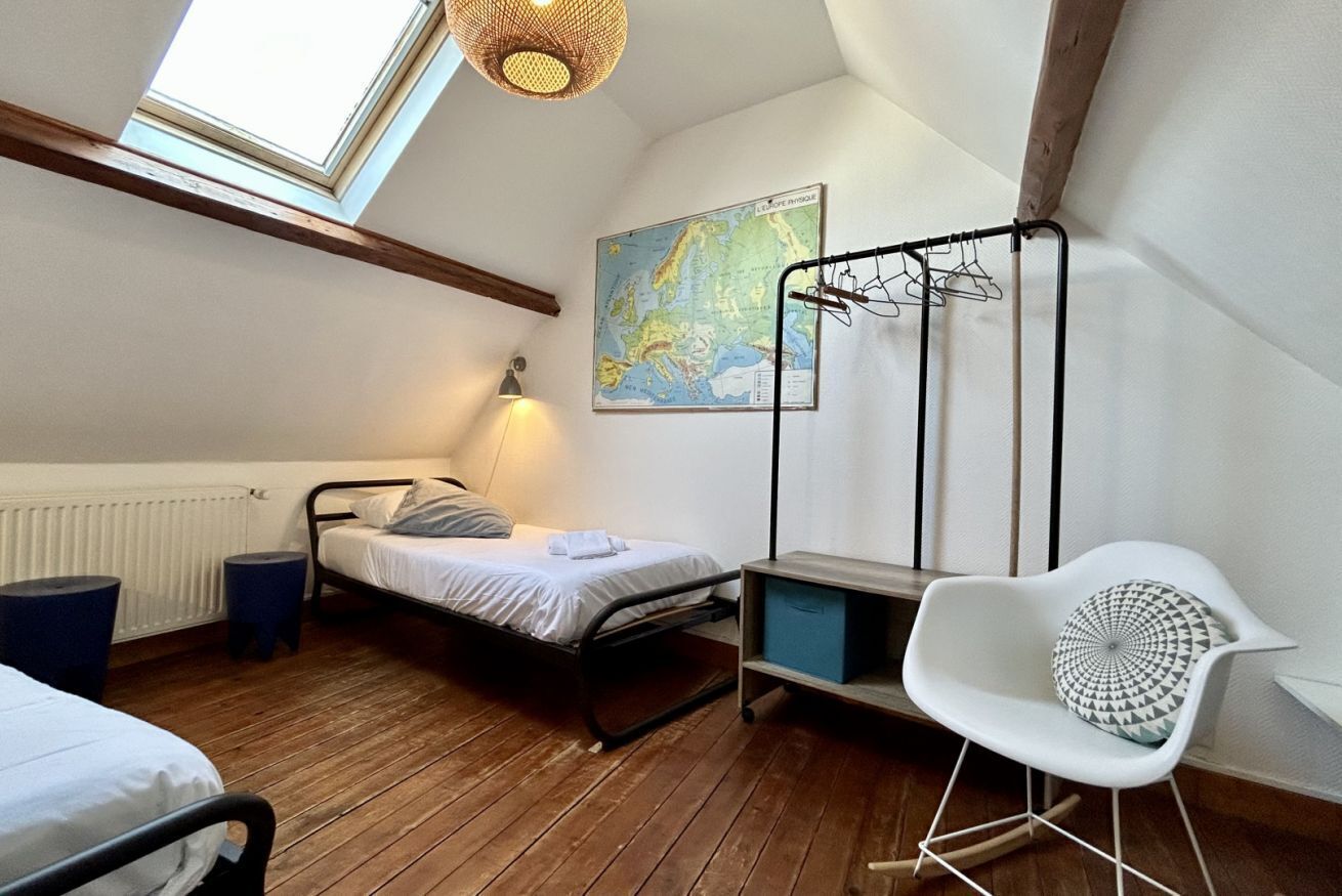 A bedroom with a bed, a map on the wall, a chair, and a hanging clothes rack.