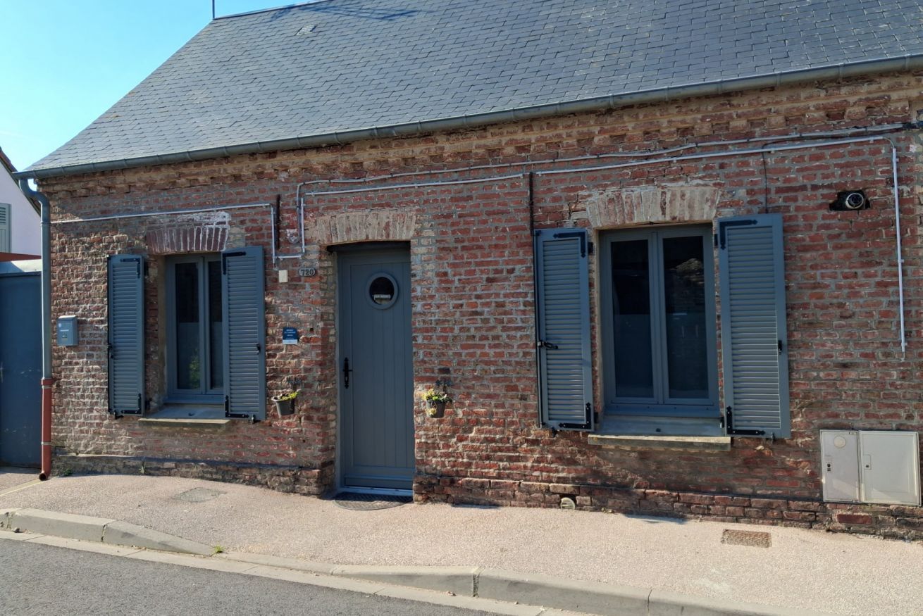 A brick building with a grey door and shutters, a small porch, and a visible window.