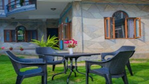 A building with a stone facade, a balcony, and a table with chairs in the foreground. - Merostay 019 Hotel Bien Venue (Pokhara)
