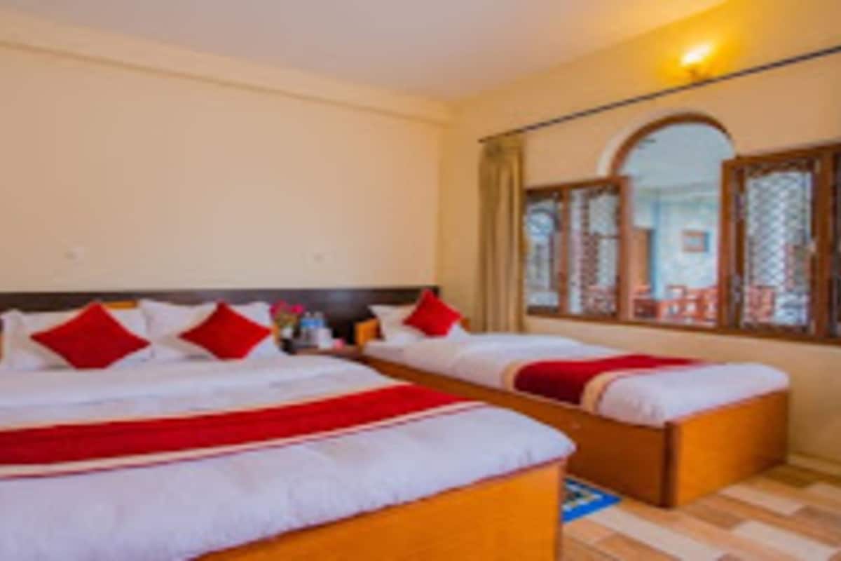 A hotel room with two beds, each with red pillows and a white bedspread.
