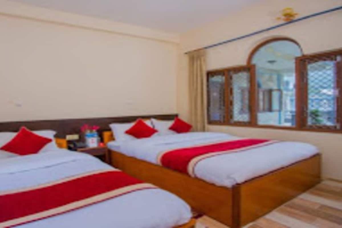 A hotel room with two beds, each with red and white bedding, a wooden headboard, and a window with a view of the outside.
