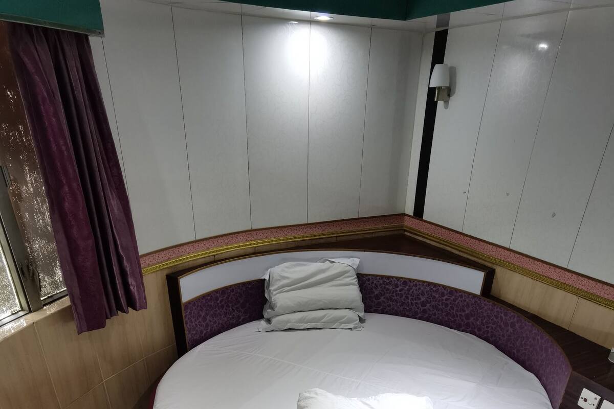 A circular bed with a red frame, white bedding, and a purple headboard.