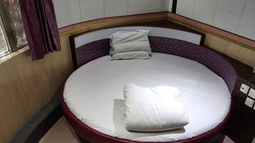 Una cama redonda con estructura roja, ropa de cama blanca y cabecera morada.