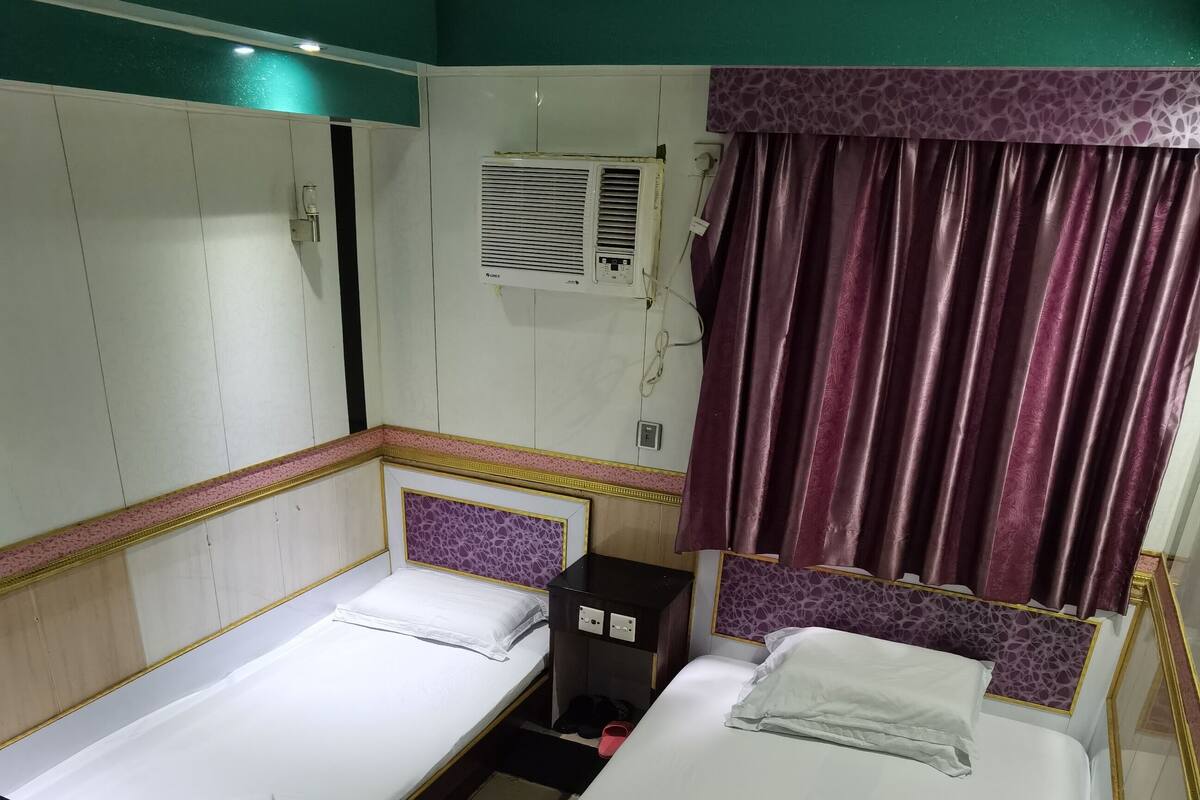 A hotel room with two single beds, a small desk, an air conditioning unit, and a purple curtain.
