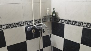 A bathroom with black and white checkered tiles, a shower with a handheld showerhead, and a small shelf with toiletries. - spanish hostel (Kowloon)