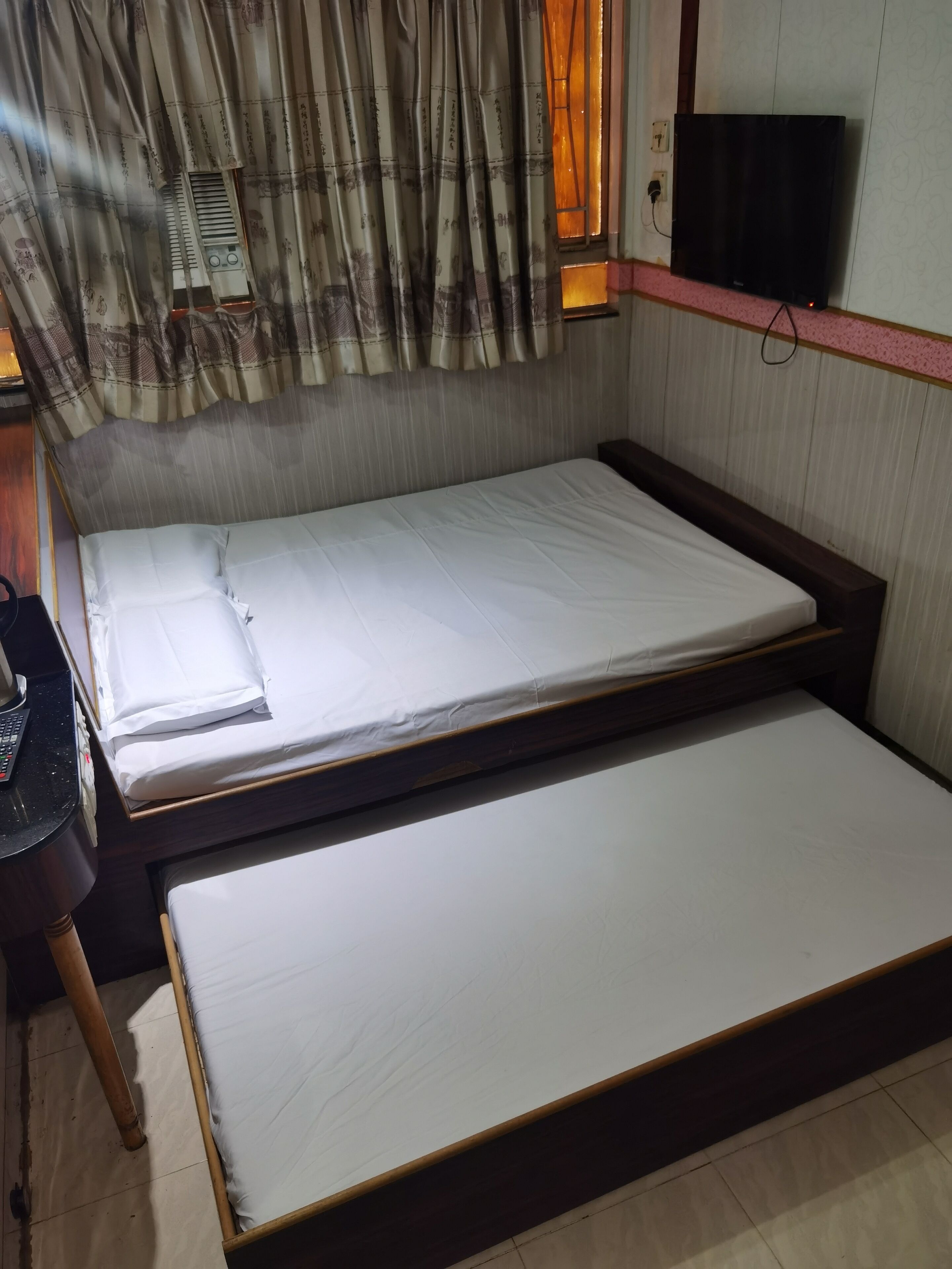 A room with a bed, a small table, a chair, a television, and a window with curtains.