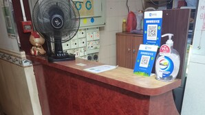 A reception desk with a red marble top, a black fan, a Hello Kitty decoration, and a Wacn hand sanitizer dispenser. - spanish hostel (Kowloon)