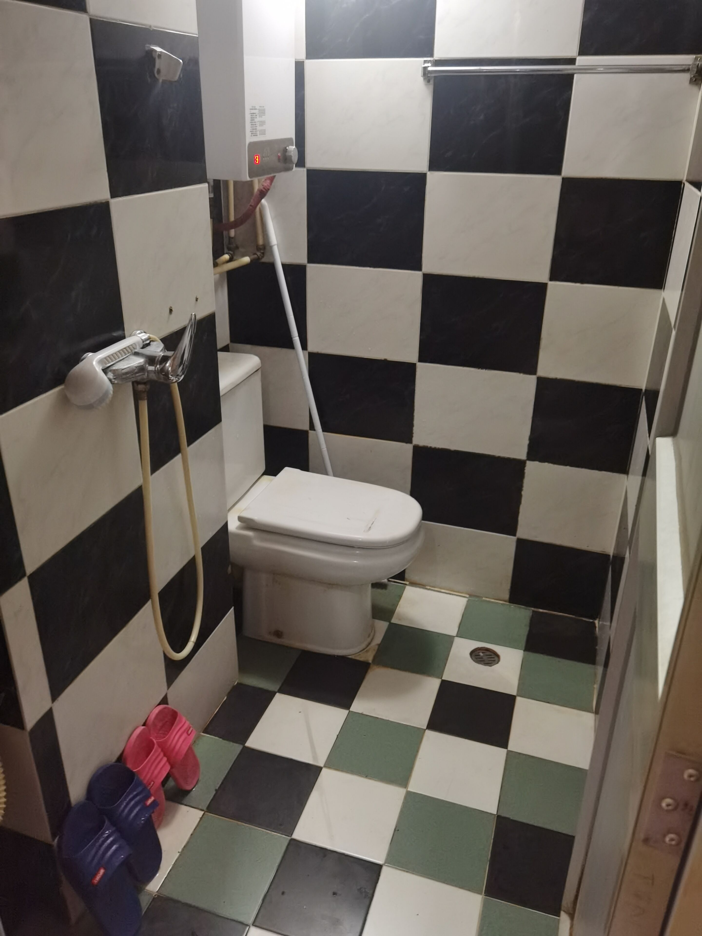 Et lille badeværelse med fliser, toilet, bruser og en håndtørrer.