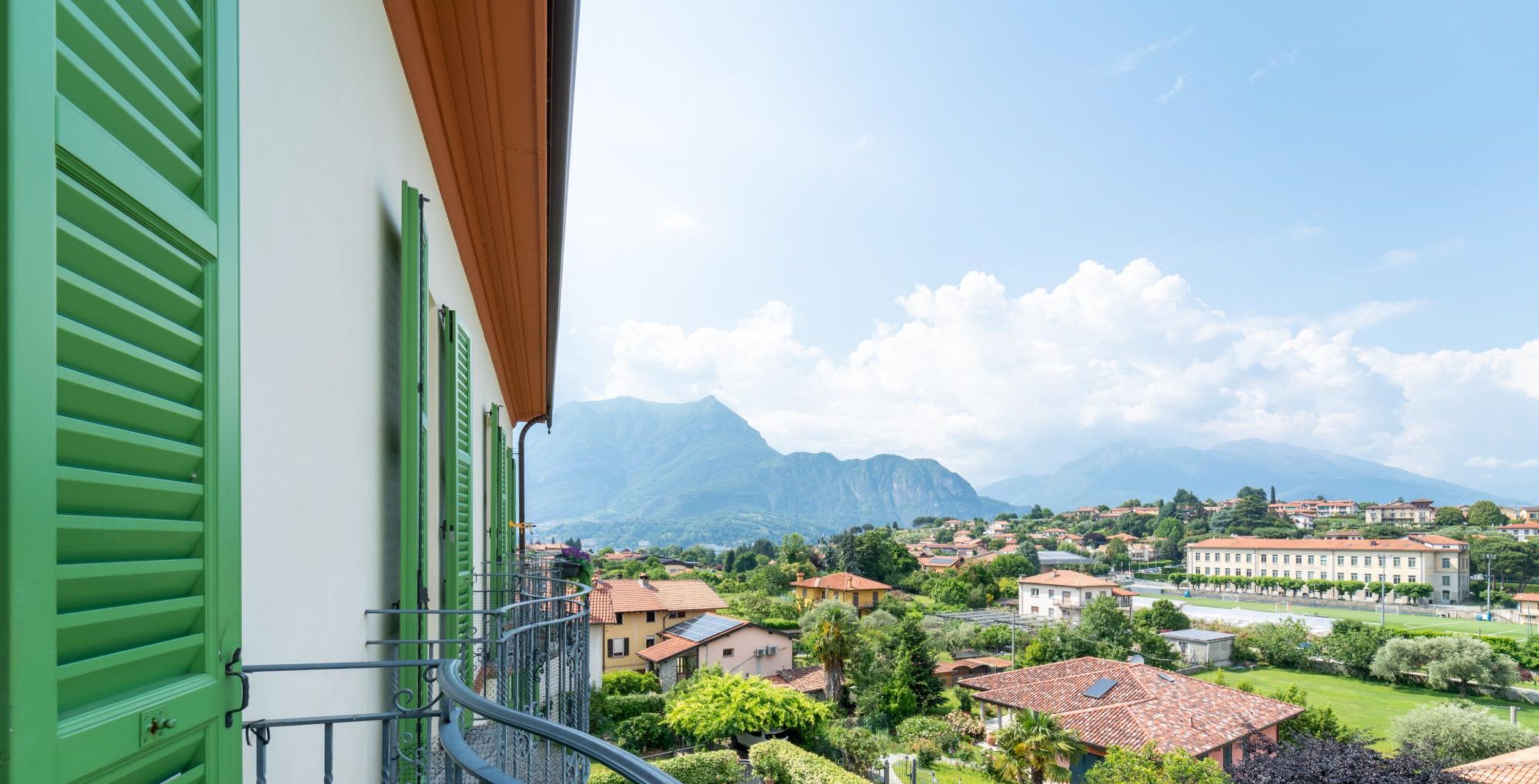 Ein Balkon mit grünen Fensterläden, der auf eine Stadt mit Bergen im Hintergrund blickt.