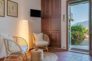 A room with wicker chairs, a TV, and a door leading to a balcony with flowers.