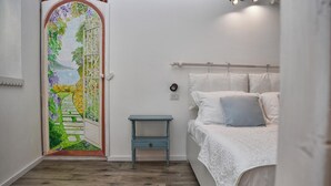 A bedroom with a bed, a small bedside table, a white door with a floral design, and a wooden floor. - Ca de Sota by Wonderful Italy (Bellagio)