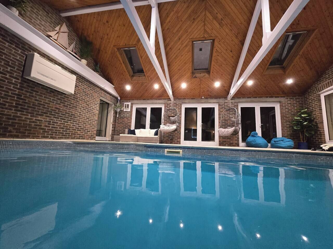 An indoor swimming pool with a wooden ceiling, brick walls, and a skylight.