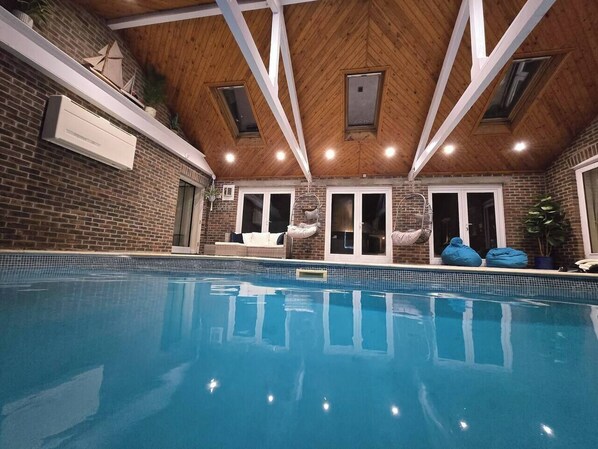 An indoor swimming pool with a wooden ceiling, brick walls, and a skylight.
