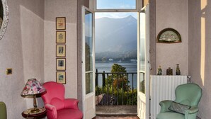A room with a large window, a pink chair, a green chair, and a table with a lamp. - Emilia Apartment by Wonderful Italy (Bellagio)
