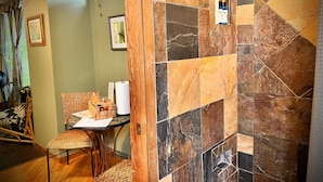 A room with a tiled wall, a wooden door, a wicker chair, a table with a basket, and a window with blinds. - Maui What A Wonderful B&B Pineapple Ste (Kihei)