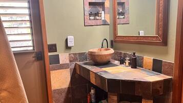 A bathroom with a wooden vanity, a large mirror, and a window with blinds.