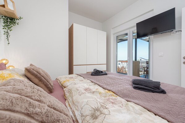A modern bedroom with a bed, a wardrobe, a television, and a balcony.