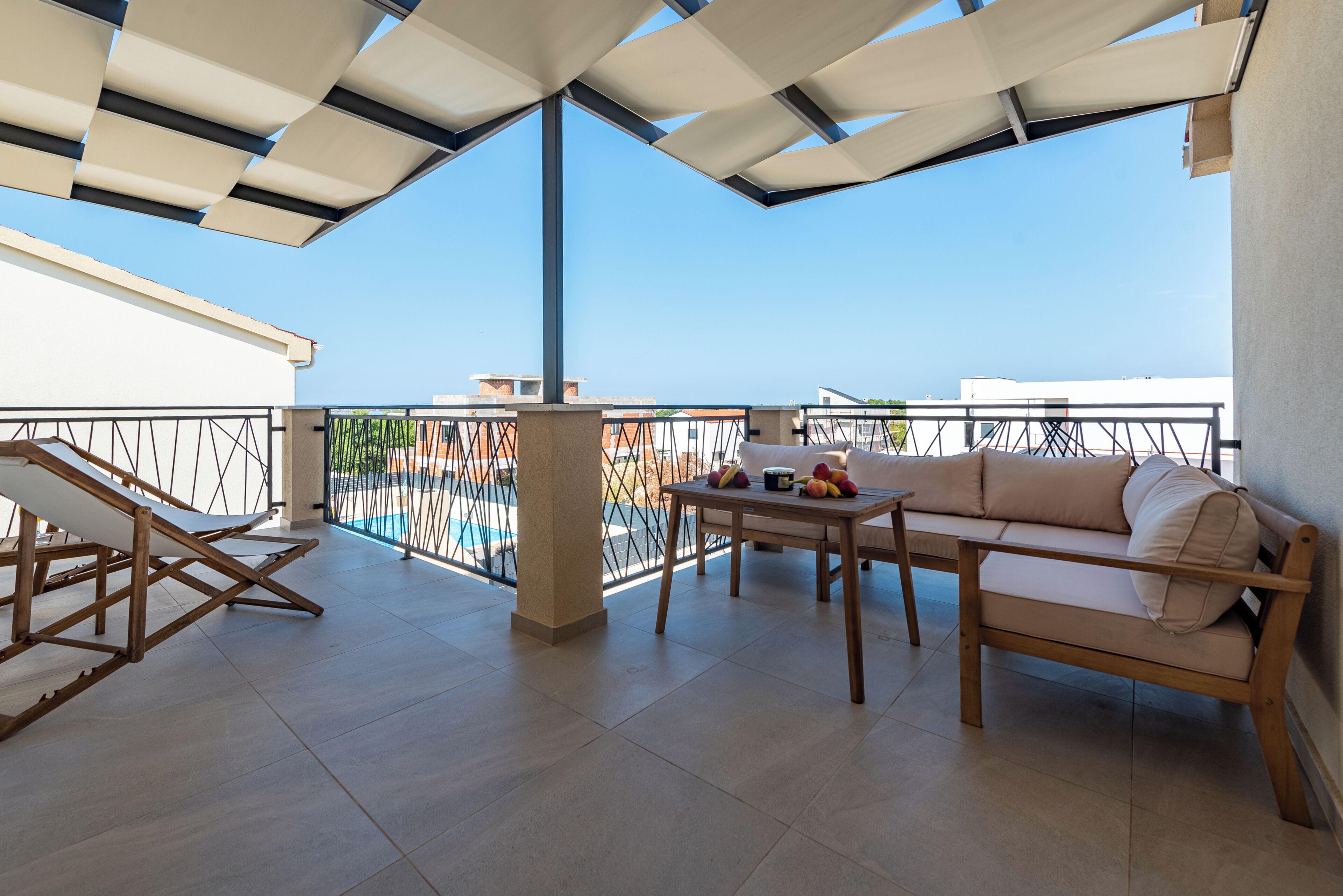 A balcony with a sofa, a table with fruit, and a pool in the background.