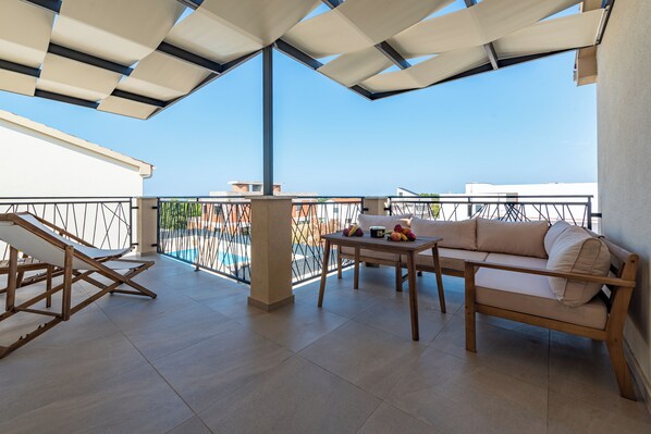 A balcony with a sofa, a table with fruit, and a pool in the background.