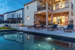 A modern two-story house with a swimming pool, outdoor seating, and a stone facade.