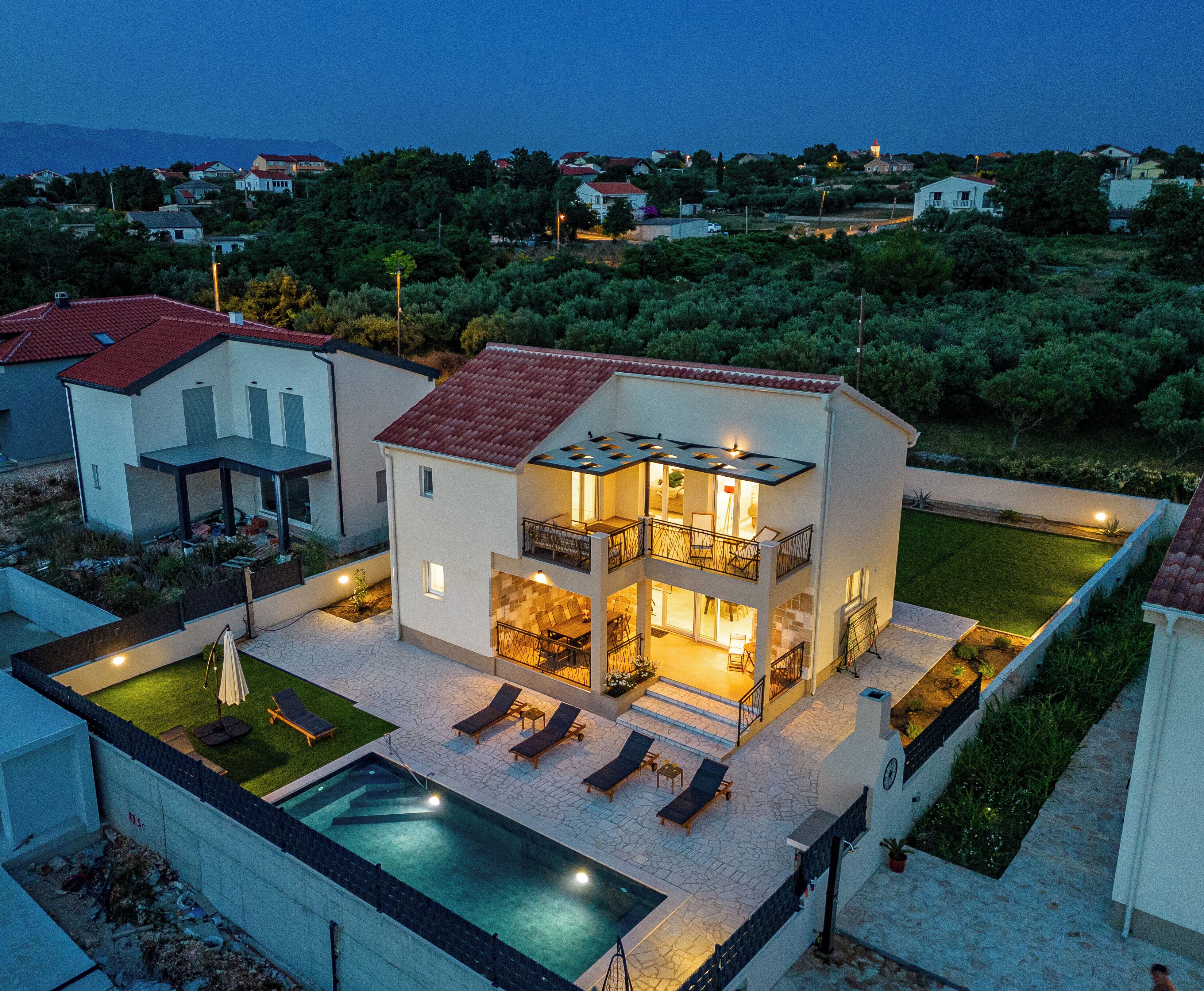 A two-story house with a swimming pool, outdoor seating, and a view of the surrounding landscape.