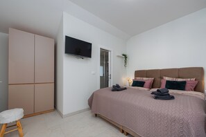 A bedroom with a bed, a television mounted on the wall, a wardrobe, and a small stool.