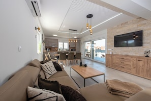 A modern living room with a sofa, coffee table, and a TV mounted on a stone wall. - Stunning Vacation Home in Vrsi—A Seaside Getaway with a Private Saltwater Pool (Vrsi)
