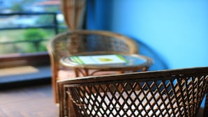 Wicker chairs and a small table on a balcony with a view of greenery. - MeroStay 020 Unique Mountain Guest House (Pokhara)
