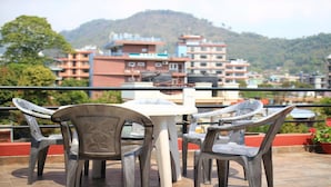 A terrace with a table and chairs, overlooking a cityscape with buildings and hills. - MeroStay 020 Unique Mountain Guest House (Pokhara)