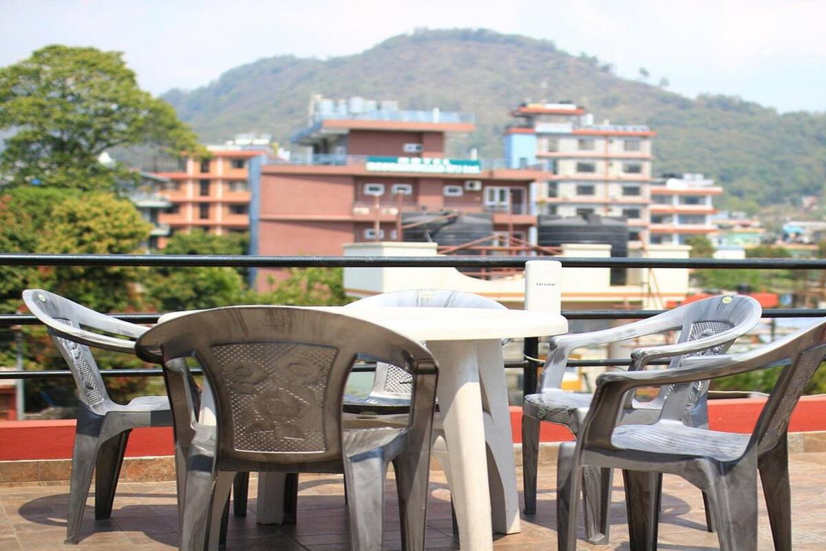 A terrace with a table and chairs, overlooking a cityscape with buildings and hills.