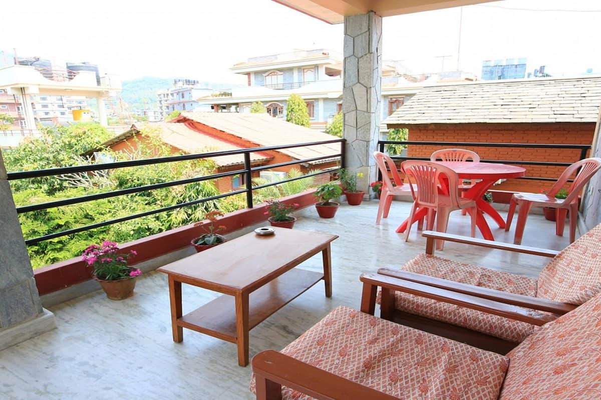 A balcony with a wooden table and chairs, potted plants, and a view of surrounding buildings.